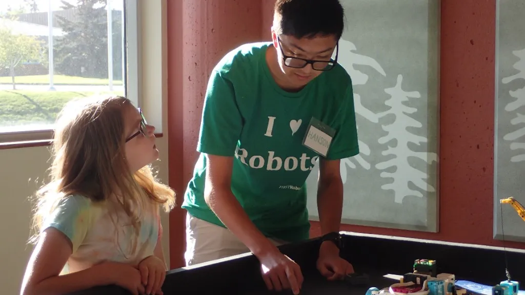 A mentor mentors a younger learner beside a robotics table during a STEM camp